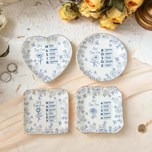 May include: Four decorative porcelain plates with blue floral patterns and gold trim. Each plate has a different shape: heart, round, square, and a scalloped square. Text and floral illustrations are printed on each plate.