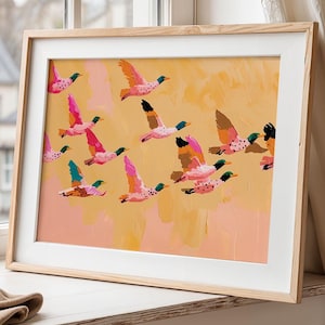 Könnte beinhalten: Ein gerahmter horizontaler Kunstdruck, der einen Schwarm stilisierter Enten im Flug vor einem warmen, pfirsichfarbenen Hintergrund zeigt. Die Enten sind in leuchtenden Rosa-, Orange- und Blaugrüntönen gehalten und weisen sichtbare Pinselstrichstrukturen auf.