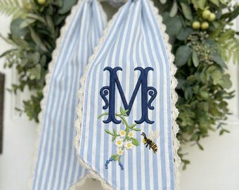 Personlig krans med bi och prästkrage, blå randig broderad monogramrosett, dekoration till verandan