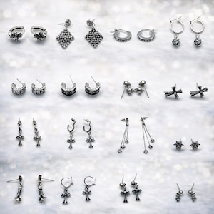 May include: A selection of silver earrings, including hoops, studs, and drop earrings. The earrings showcase cross, star, and geometric patterns. The jewellery is presented on a white, textured surface.