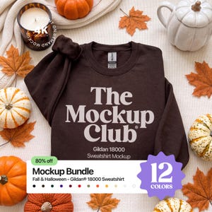May include: A dark brown crewneck sweatshirt featuring the white text The Mockup Club and Gildan 18000 Sweatshirt Mockup. The garment is displayed with a scrunchie on the sleeve, surrounded by decorative pumpkins and autumn leaves on a white fabric.