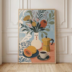 May include: A framed art print featuring a light blue background with a white vase shaped like a face holding a bouquet of flowers. A yellow moka pot, a cup of coffee on a saucer, and a sliced papaya on a blue plate sit on a red table.