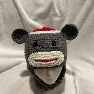 May include: Gray crocheted monkey hat with red and white details. The hat has a long neck warmer attached.