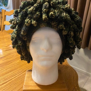 May include: A green, black, and brown crocheted hat with a curly, afro-like style.