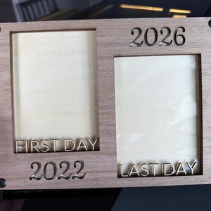 Könnte beinhalten: Ein rechteckiger doppelter Bilderrahmen aus Holz mit hellbrauner Holzmaserung. Auf der linken Seite steht der Text FIRST DAY und 2022, während auf der rechten Seite 2026 und LAST DAY zu sehen sind. Vier schwarze runde Befestigungen sind an den Ecken.