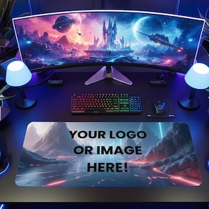 Peut inclure: Une configuration de jeu avec un &eacute;cran incurv&eacute; affichant un paysage fantastique, un clavier, une souris et un tapis de souris avec le texte "YOUR LOGO OR IMAGE HERE!". L'ensemble comprend des lampes, des haut-parleurs et un casque, tous &eacute;clair&eacute;s en bleu et violet.