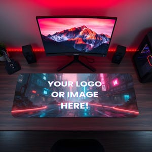 May include: A rectangular gaming mouse pad with the text "YOUR LOGO OR IMAGE HERE!" is displayed on a wooden desk. The pad features a neon city scene with a mountain-themed computer monitor, speakers, and a computer tower.