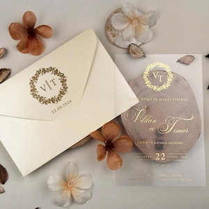 Puede incluir: Juego de invitaciones de boda en marfil con detalles dorados. El sobre presenta un monograma y una fecha. También hay una tarjeta transparente con escritura dorada y un diseño de rodaja de madera, con decoraciones florales.