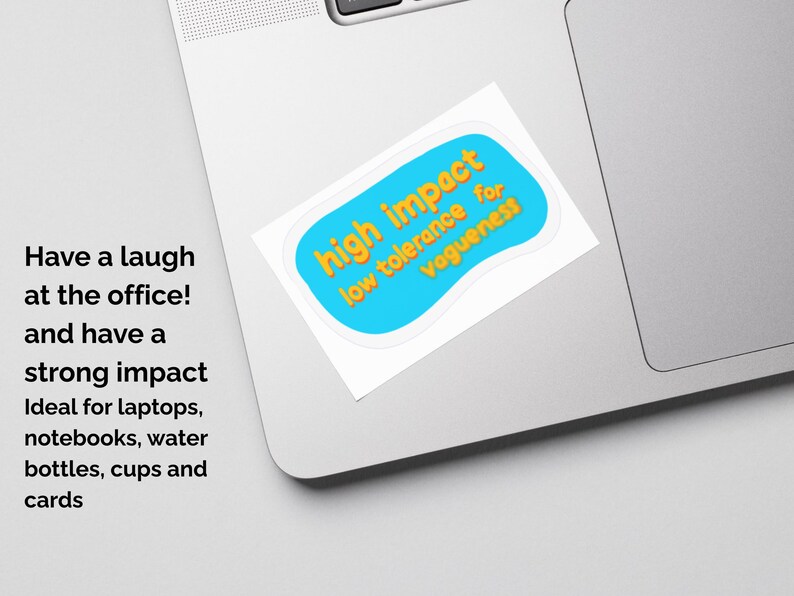 May include: A sticker on a laptop with the text "high impact low tolerance for vagueness" in orange on a blue background. The sticker is white-bordered and is on a silver laptop.