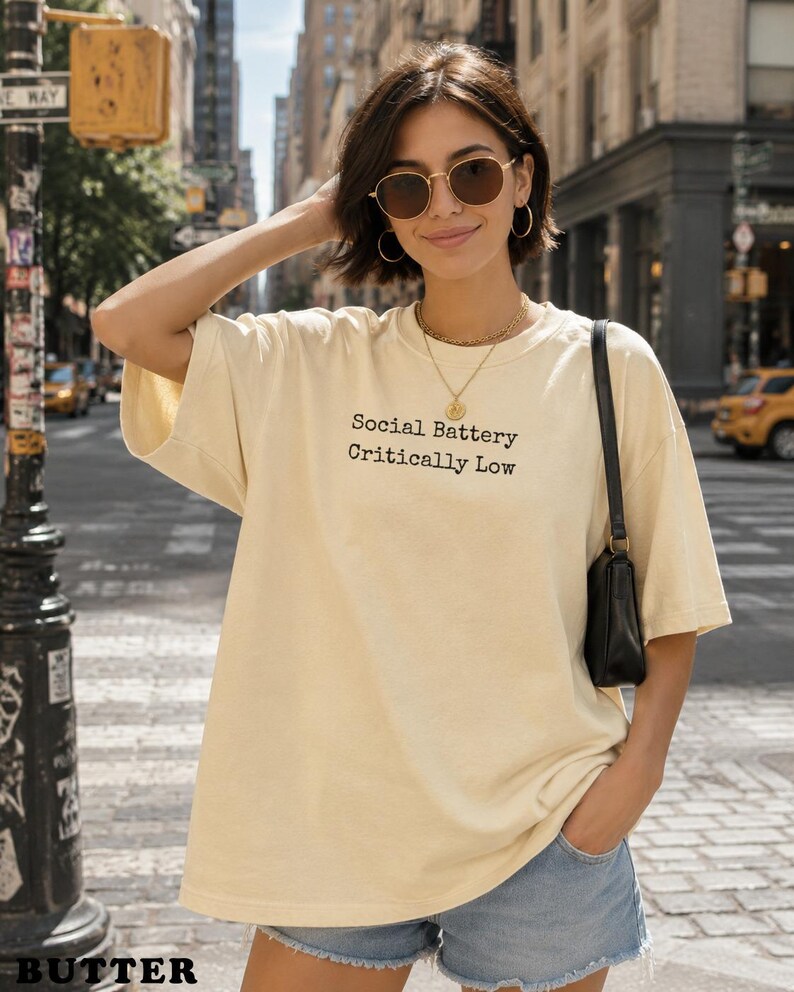Woman wearing a cream t-shirt with "Social Battery Critically Low" text.