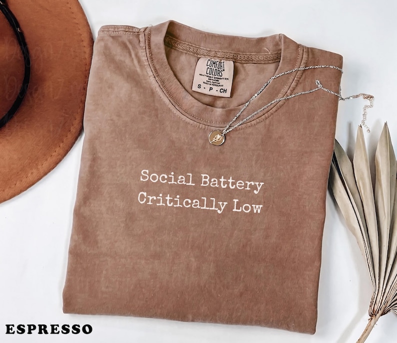 Brown t-shirt with "Social Battery Critically Low" text and espresso label.