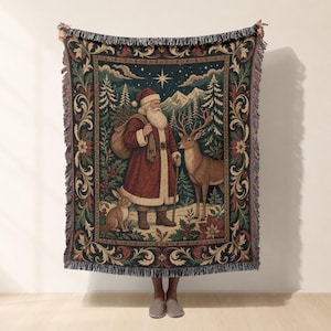 Puede incluir: Una manta tejida que presenta una escena detallada de Santa Claus con abrigo rojo y un saco, de pie en un bosque nevado con un ciervo y un conejo. El diseño incluye una estrella en el cielo nocturno, pinos y un borde floral decorativo.