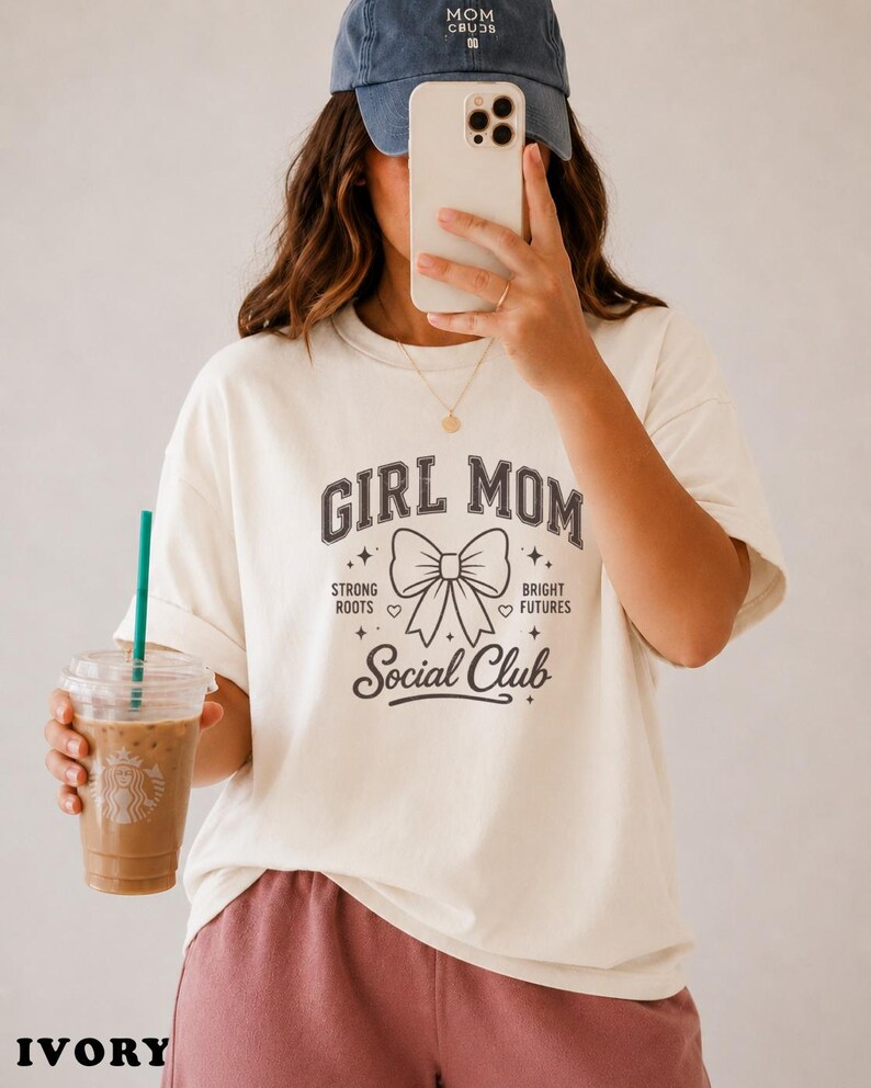Woman in cream t-shirt with "Girl Mom Social Club" text, holding iced coffee.