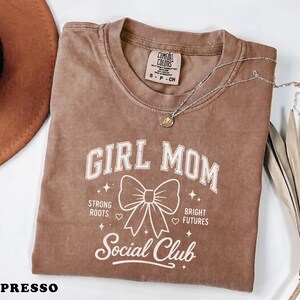 Brown Comfort Colors "Girl Mom" t-shirt with "Strong Roots, Bright Futures" and a bow.