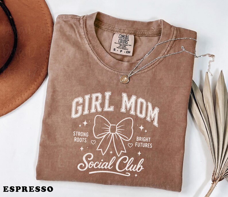 Brown Comfort Colors "Girl Mom" t-shirt with "Strong Roots, Bright Futures" and a bow.