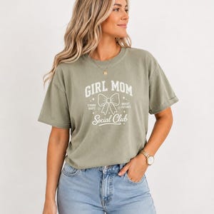 Woman wearing a light green t-shirt with "Girl Mom Social Club" text.