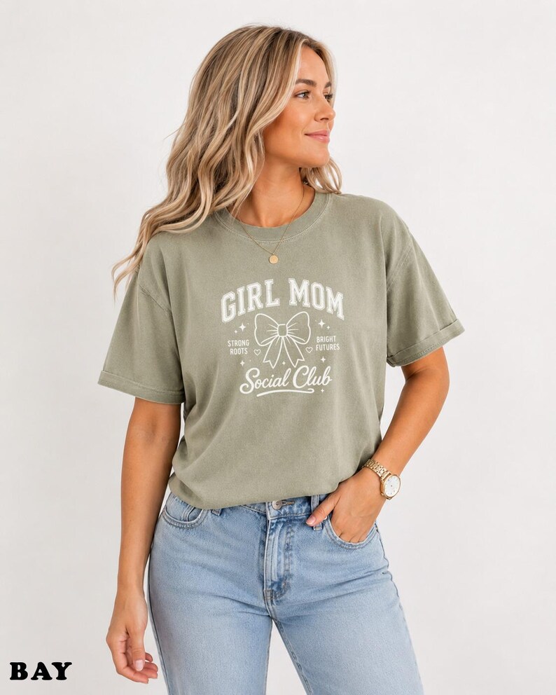 Woman wearing a light green t-shirt with "Girl Mom Social Club" text.