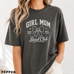 Dark grey t-shirt with "GIRL MOM SOCIAL CLUB" text and a bow graphic.