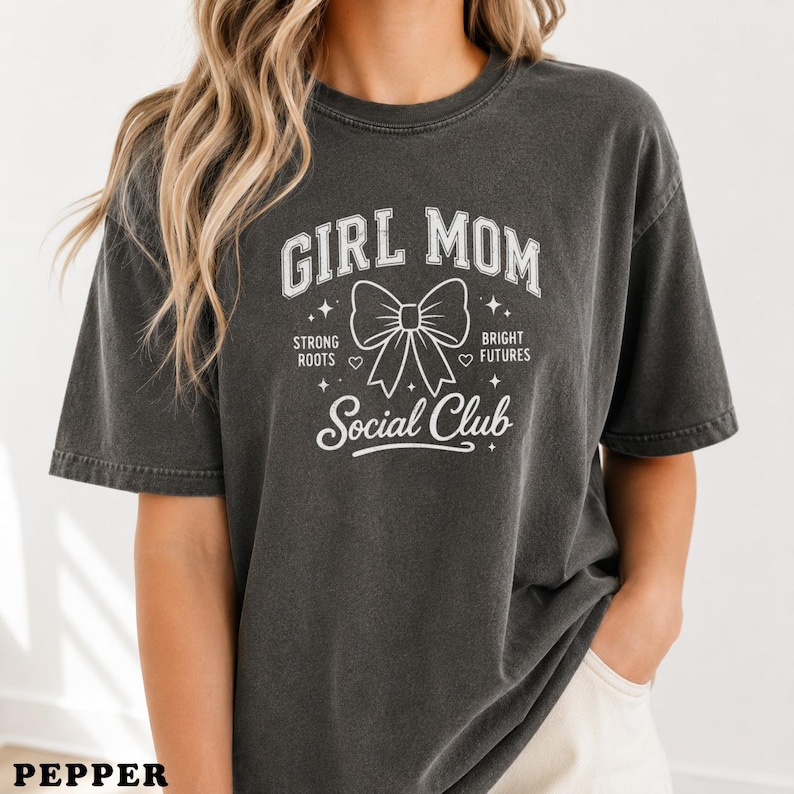 Dark grey t-shirt with "GIRL MOM SOCIAL CLUB" text and a bow graphic.