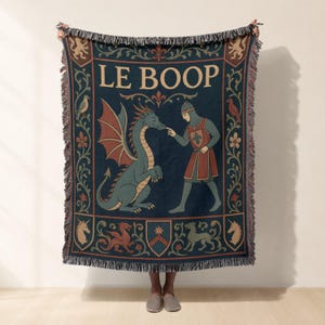 Könnte beinhalten: Eine dunkelblaue Webdecke mit einer mittelalterlichen Illustration, die einen Ritter zeigt, der die Nase eines Drachen berührt. Der Text LE BOOP steht oben. Der Rand ist mit Blumenmotiven, heraldischen Wappen und Fabelwesen verziert.