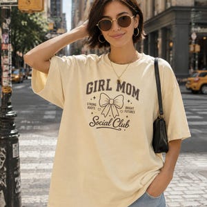 Cream t-shirt with "Girl Mom" text and bow graphic.