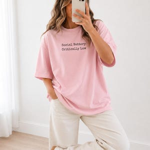 Pink t-shirt with "Social Battery Critically Low" text, worn by a woman.