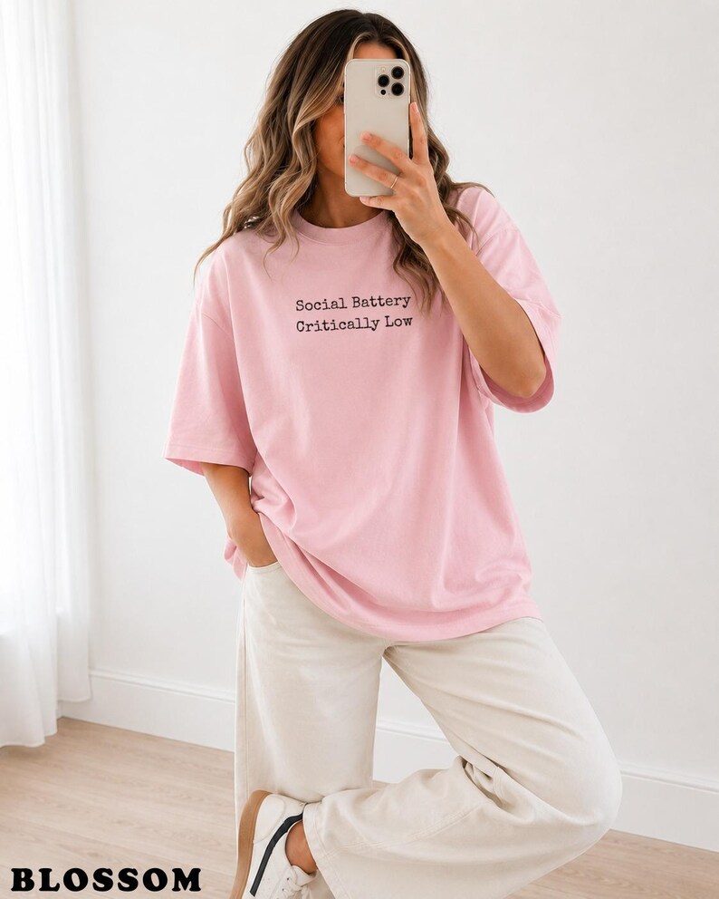Pink t-shirt with "Social Battery Critically Low" text, worn by a woman.