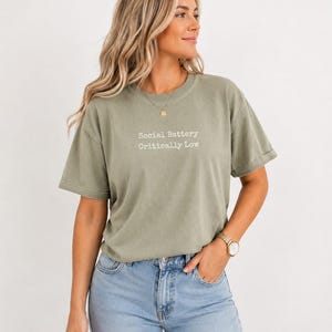 Light green t-shirt with "Social Battery Critically Low" text, worn by a woman.