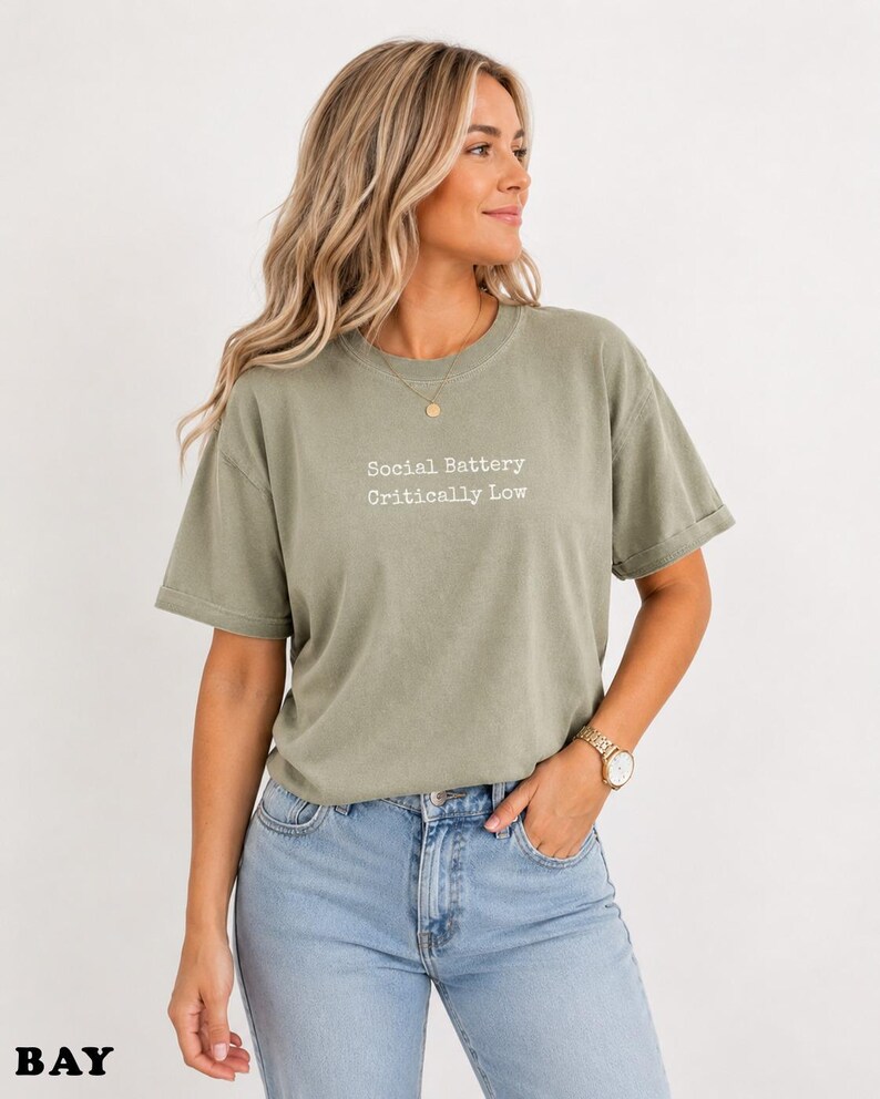 Light green t-shirt with "Social Battery Critically Low" text, worn by a woman.