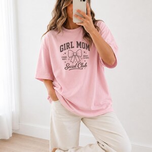 Pink t-shirt with "Girl Mom Social Club" graphic, worn by a woman.