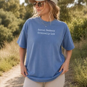Woman wearing blue t-shirt with "Social Battery Critically Low" text.