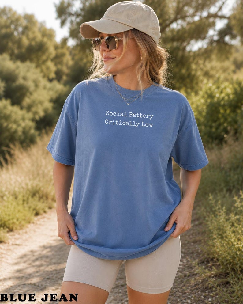 Woman wearing blue t-shirt with "Social Battery Critically Low" text.