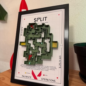 May include: Framed artwork showing a 3D map of the "Split" battleground from a video game. The map is green with red accents, set against a white background with text. The frame is black.