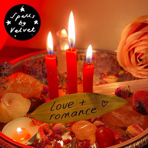 May include: Three lit red taper candles arranged on a silver tray with crystals, dried rosebuds, and a bay leaf inscribed with the text love + romance. A small tea light candle glows nearby, and a large peach-coloured rose sits on the right side.