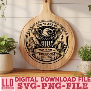 May include: A round wooden cutting board with a handle, featuring a black graphic design commemorating 250 years of freedom. The design includes an eagle, the Statue of Liberty, and the Liberty Bell. The text reads "250 Years of Freedom 1776-2026."
