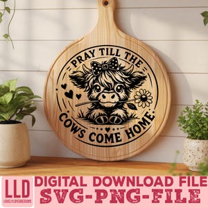 May include: A round wooden cutting board with a handle, featuring a black and white illustration of a Highland cow with a flower in its mouth. The text "PRAY TILL THE COWS COME HOME" is inscribed around the cow. Below the board is text that reads "DIGITAL DOWNLOAD FILE SVG-PNG-FILE".