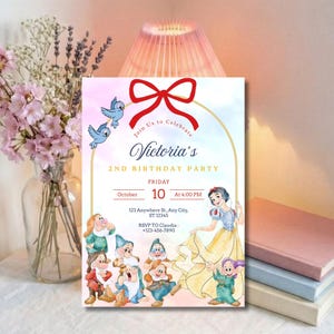以下が含まれることがあります： 「Victoria's 2nd Birthday Party」のテキストが入った誕生日パーティーの招待状。赤いリボン、青い鳥、白雪姫と七人の小人のイラストがデザインされています。日付と時間も含まれています。