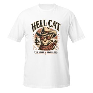 May include: A white t-shirt featuring a graphic of a leopard wearing a cowboy hat and sunglasses, with a bandana around its neck. The text HELL CAT appears above, and WILD HEART COWGIRL SOUL appears below, surrounded by a desert landscape illustration.