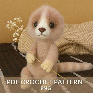 May include: A handmade crochet meerkat toy in shades of pink and cream, with large black eyes and a brown nose. The meerkat is holding a sprig of white flowers. The text "PDF CROCHET PATTERN ENG" is at the bottom of the image.