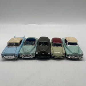 Peut inclure: Une collection de cinq voitures miniatures alignées côte à côte. L'ensemble comprend une voiture bleu clair avec un toit crème, un cabriolet vert clair, une berline noire mate, une voiture crème avec un toit rouge et une voiture vert clair avec un toit crème.