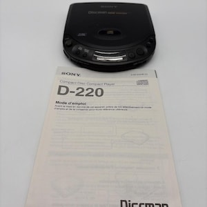 Pode incluir: Um leitor de CD portátil Sony Discman preto com botões de controlo circulares e um compartimento central para discos, acompanhado por um manual de instruções branco com o texto Compact Disc Compact Player D-220 e Sony Corporation 1993.