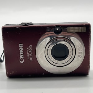 Op de afbeelding: Een bordeauxrode Canon Digital IXUS 80 IS compactcamera met een 8,0 megapixel sensor en een Canon Zoom Lens 3x IS 6,2-18,6 mm 1:2,8-4,9. De voorzijde toont de merknaam, het modelnummer en de technische specificaties van de lens.