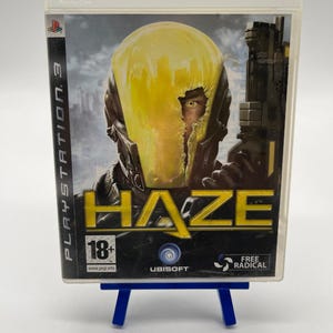 Può includere: Una custodia per videogioco PlayStation 3 del gioco Haze. La copertina raffigura un soldato con un casco scuro e una visiera gialla incrinata, che impugna un'arma. Il titolo Haze è stampato in grandi lettere gialle. Include il logo 18+.