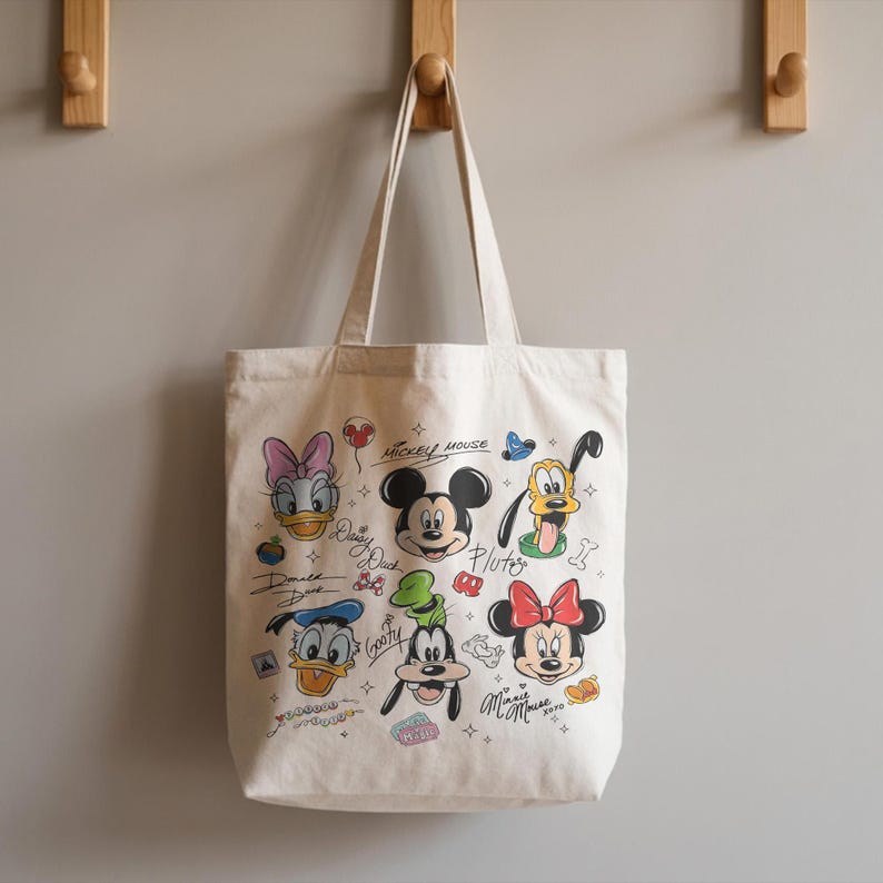 May include: Off-white canvas tote bag featuring colorful illustrations of Disney characters, including Mickey Mouse, Minnie Mouse, Donald Duck, and Pluto. The bag has two handles and is hanging on a wooden hook.