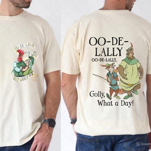 Puede incluir: Camiseta color crema con un gallo de dibujos animados tocando un laúd con el texto "OO-DE-LALLY" y "Golly, What a Day!". La parte posterior de la camiseta muestra un zorro de dibujos animados, un oso y el texto "OO-DE-LALLY, Golly, What a Day!"