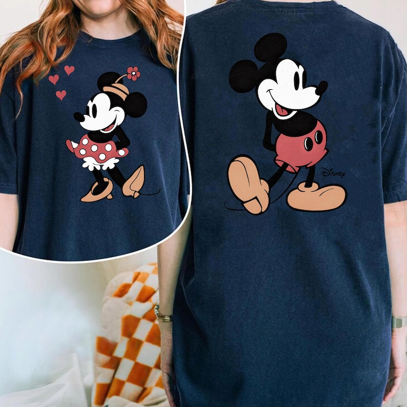 Puede incluir: Camiseta azul marino con Minnie Mouse en la parte delantera y Mickey Mouse en la trasera. Minnie lleva un vestido de lunares rojos y un sombrero de flores. Mickey lleva pantalones cortos rojos. El logotipo de Disney es visible.