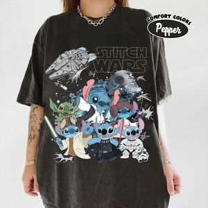 May include: Dark gray t-shirt featuring a graphic of Stitch characters in Star Wars-themed costumes. The design includes the text "STITCH WARS" and a Comfort Colors logo. The shirt has a vintage, worn look.