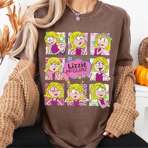 May include: Brown t-shirt featuring a grid of nine images of a cartoon character with blonde hair and a pink outfit. The text "Lizzie McGuire" is in a pink cloud. The shirt has short sleeves.