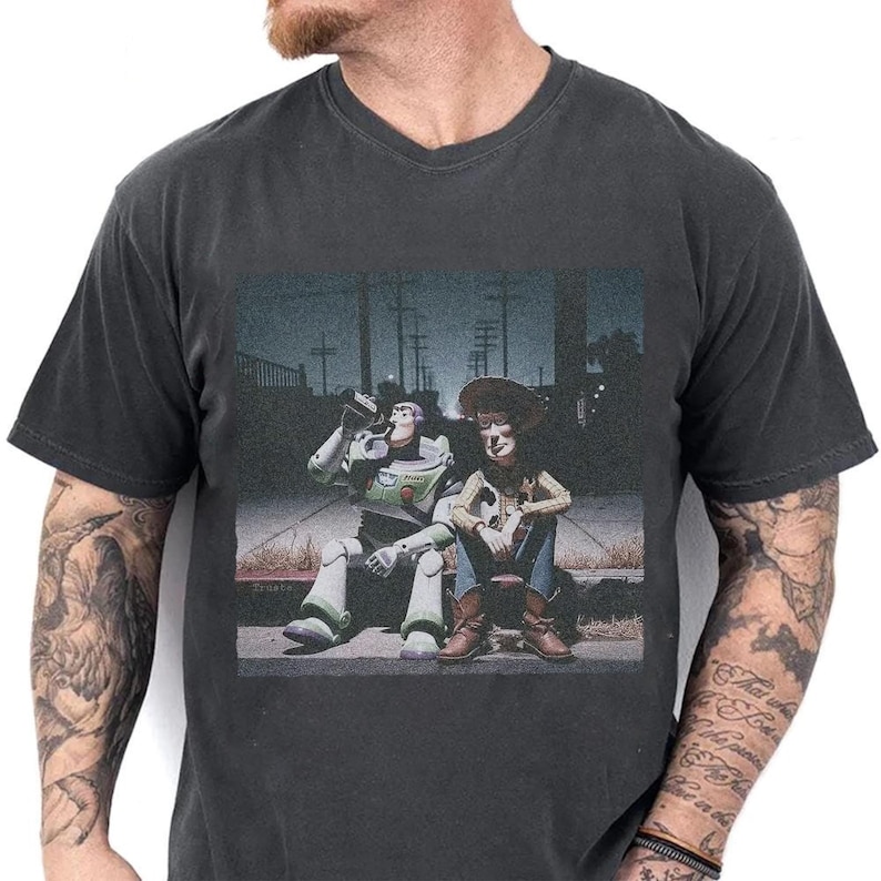 May include: Dark gray v-neck t-shirt featuring a graphic of Buzz Lightyear and Woody from Toy Story sitting together. Buzz is drinking from a bottle. The image has a vintage, slightly faded look.