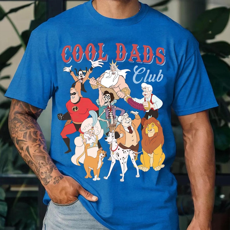 K&ouml;nnte beinhalten: Blaues T-Shirt mit dem Text "COOL DADS Club" in Rot und Wei&szlig;. Das Shirt zeigt Zeichentrickfiguren wie Mr. Incredible, Goofy und Simba. Das Shirt ist aus einem weichen Material gefertigt.